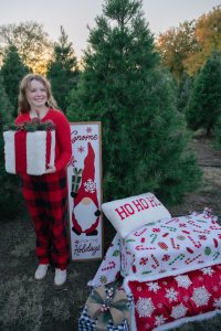girl standing next to a christmas tree with present